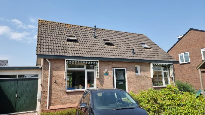 Bungalow met een grijs dak en groene deur, omringd door een tuin en andere huizen.